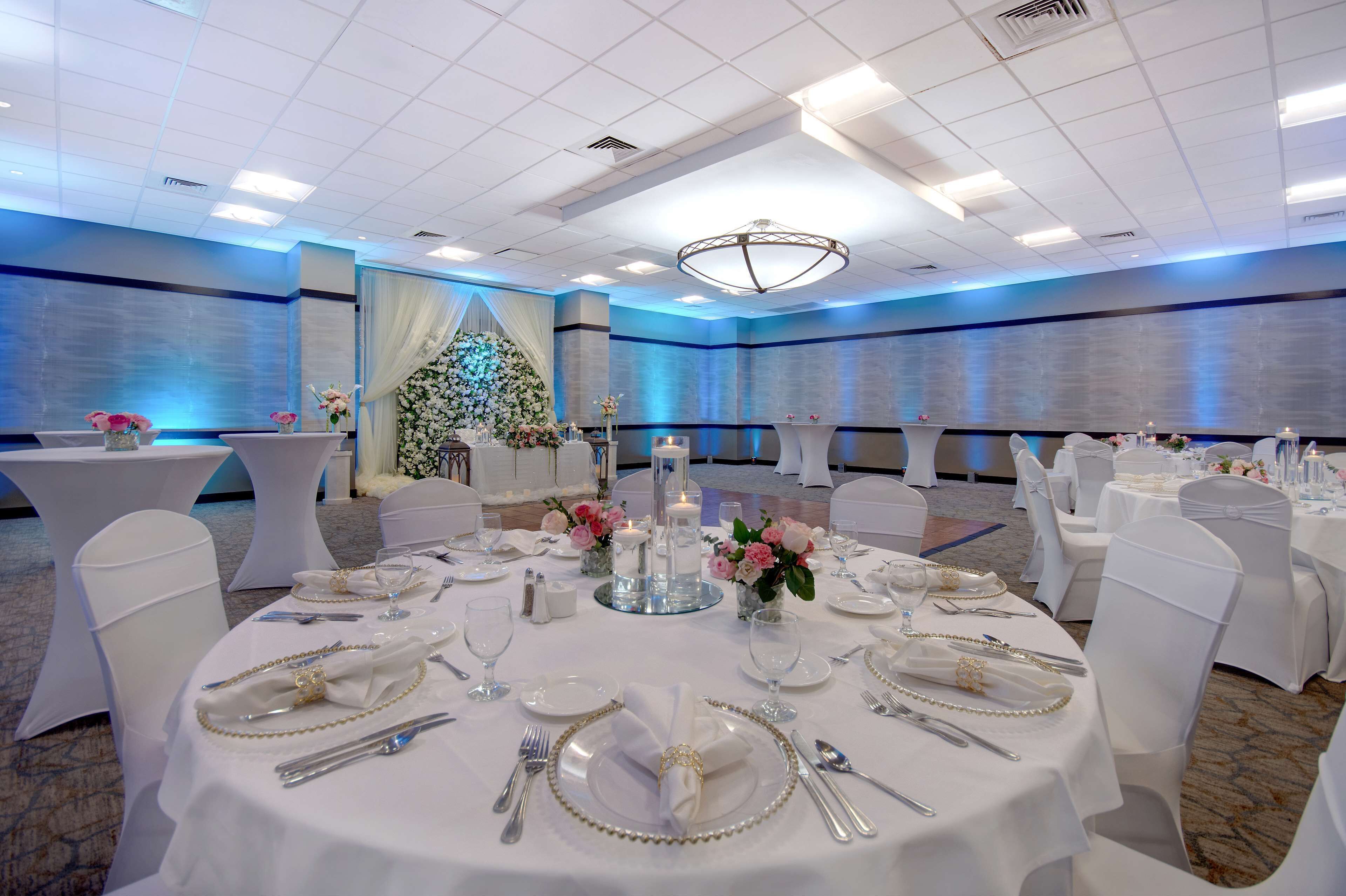 A banquet hall with round tables set for a formal event, featuring white tablecloths, glassware, and floral centerpieces.