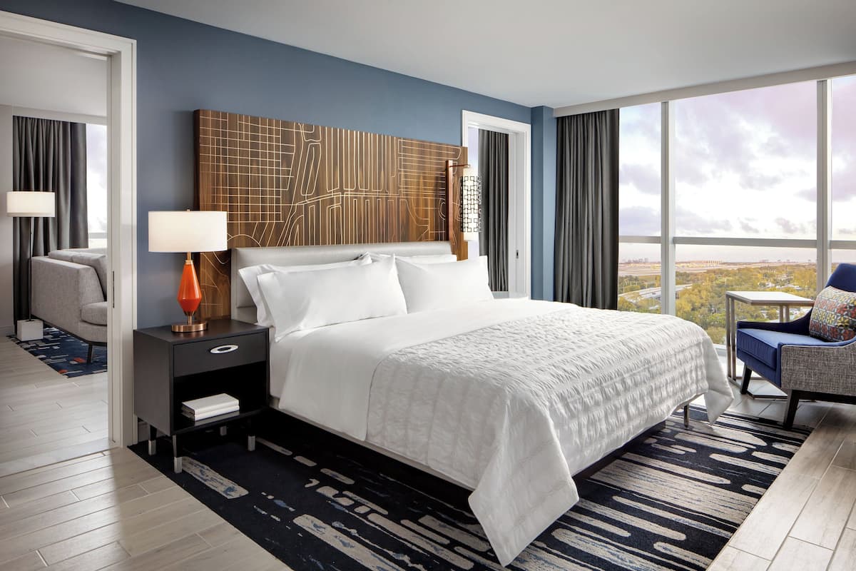A modern hotel room with a large bed, a desk, a chair, and a view of the city.