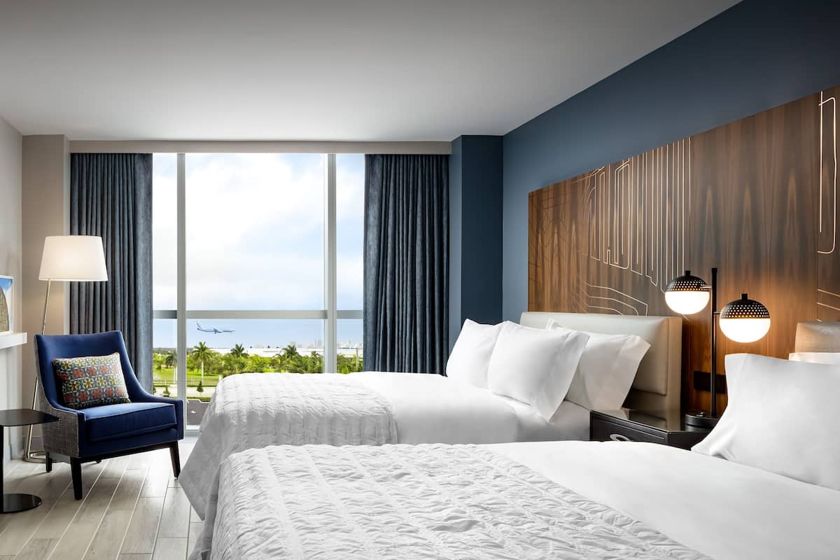 A hotel room with two beds, a view of the ocean, and a modern decor.