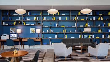 Une bibliothèque moderne avec un mur bleu, des étagères en bois, un canapé gris et une table ronde en bois.