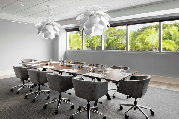 A conference room with a large table, grey chairs, and a modern chandelier.