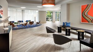 Un vestíbulo espacioso con diseño moderno, que cuenta con una zona de estar con sofás y sillones, una mesa de recepción y un cuadro abstracto de gran tamaño en la pared.