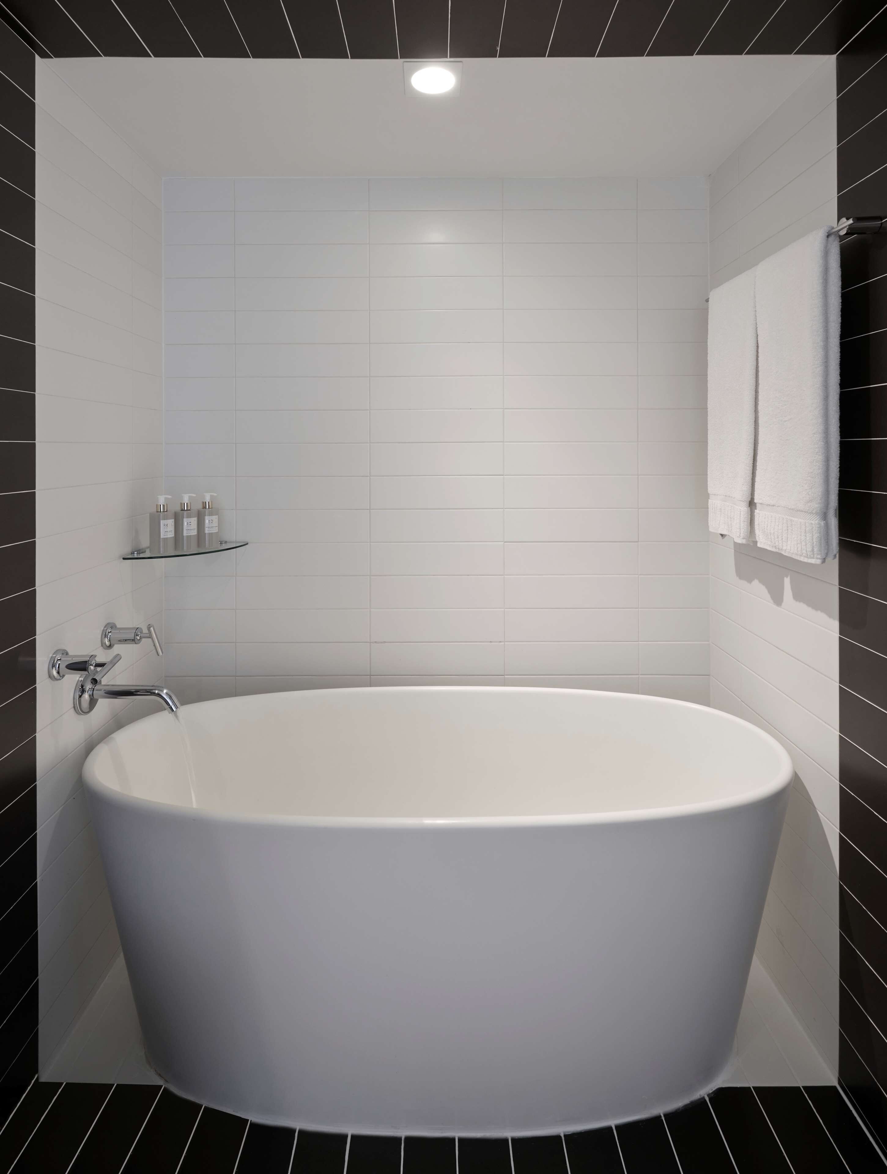 A modern bathroom with a freestanding bathtub, white tiled walls, and a glass shelf with toiletries.
