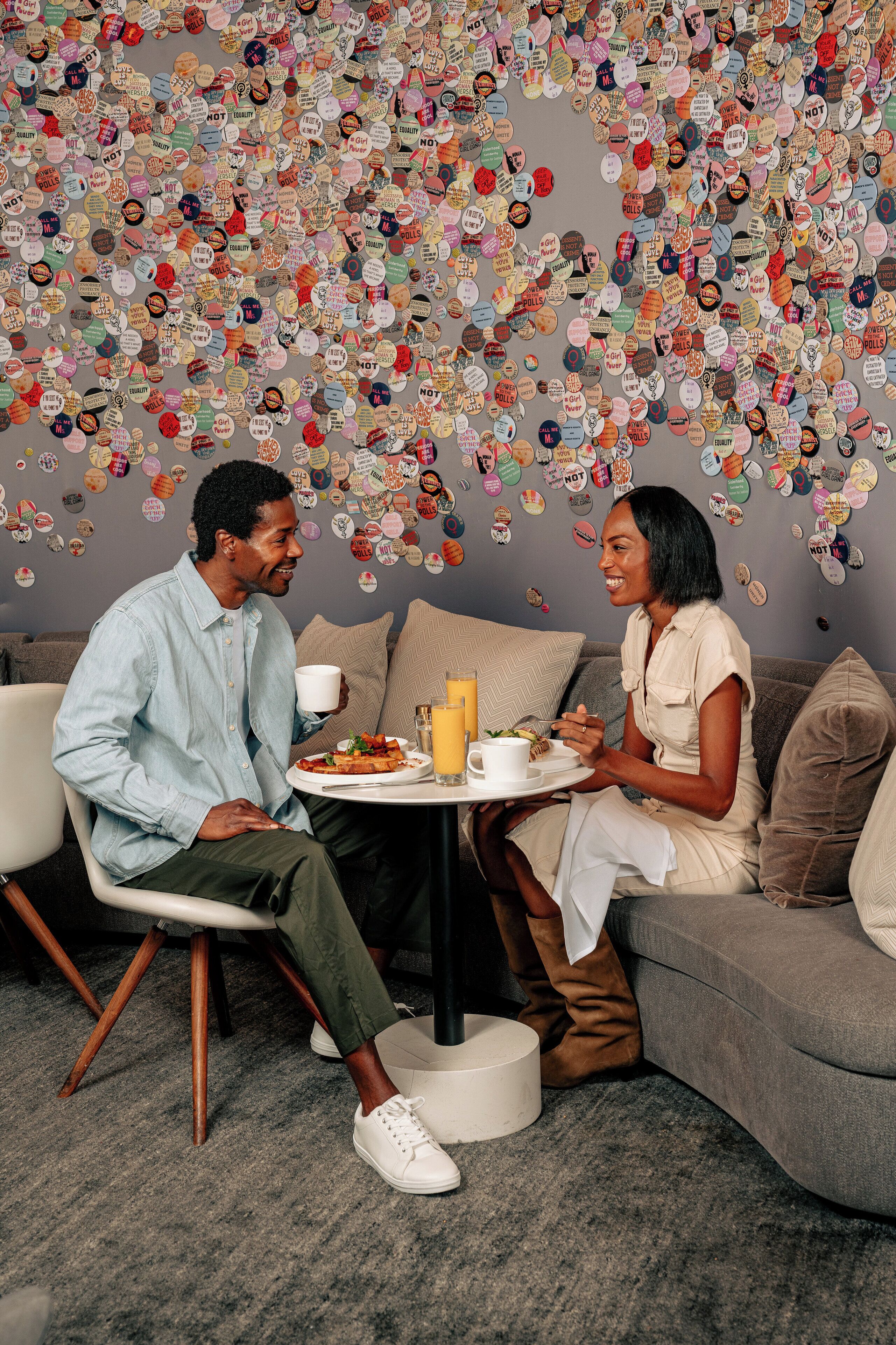 A room with a gray couch, a round table with a white cup and a plate of food, and a wall decorated with various circular stickers.