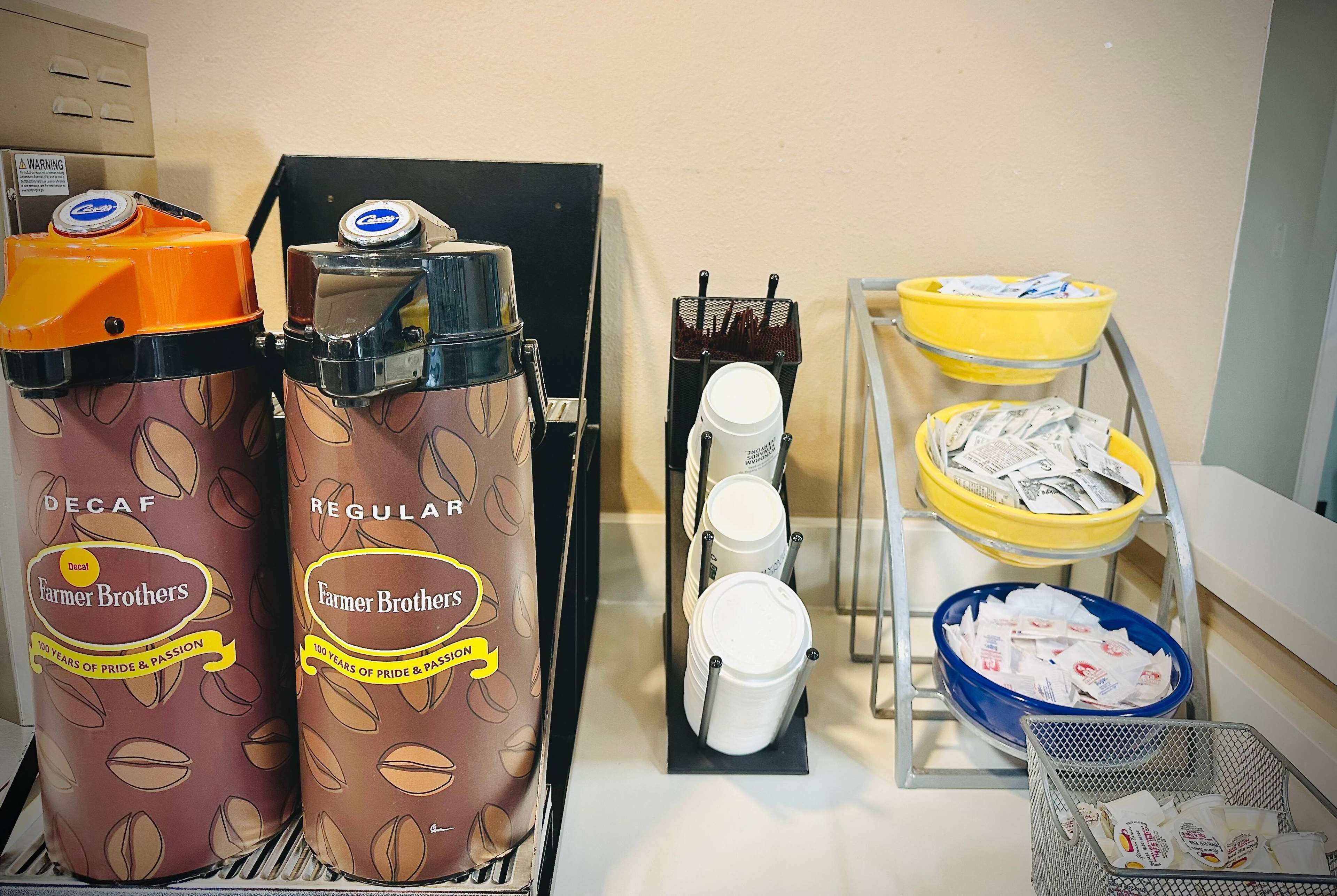 A coffee station with two coffee dispensers labeled 'DECAF' and 'REGULAR', a coffee machine, and multiple coffee cups and filters.