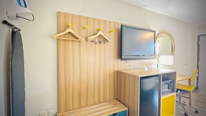 Une chambre d’hôtel avec un mur revêtu de panneaux en bois, un téléviseur à écran plat, un miroir, un bureau avec une chaise et une petite kitchenette.