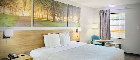 Una habitación de hotel con una cama grande, una mesita de noche con teléfono, una silla, una pequeña mesa y una ventana con cortinas.