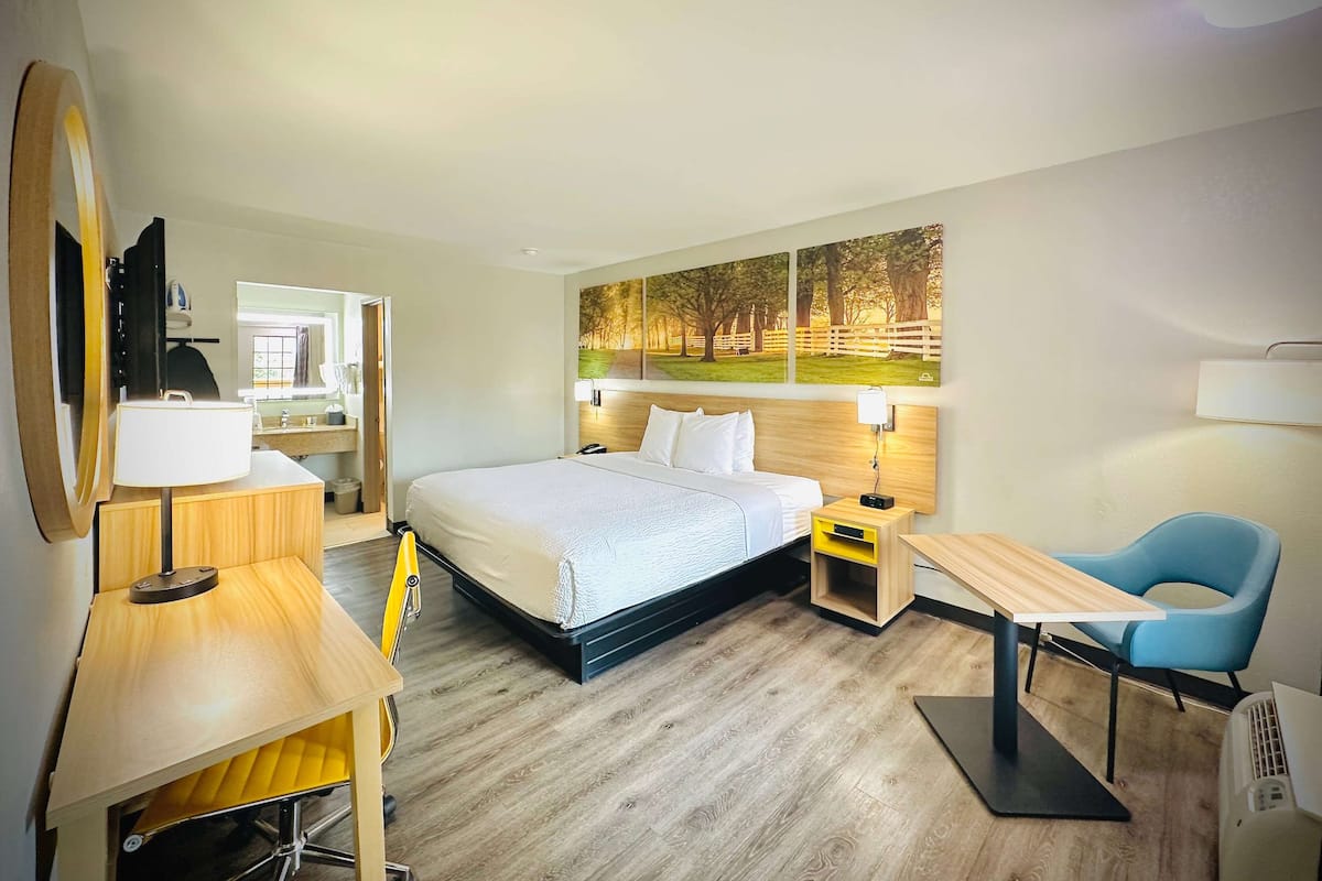 A hotel room with a bed, bedside tables, a desk, a chair, a mirror, and a painting on the wall.