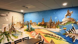 Une fresque représentant des monuments célèbres orne un mur dans un espace de restauration, où se trouvent une table et des chaises.