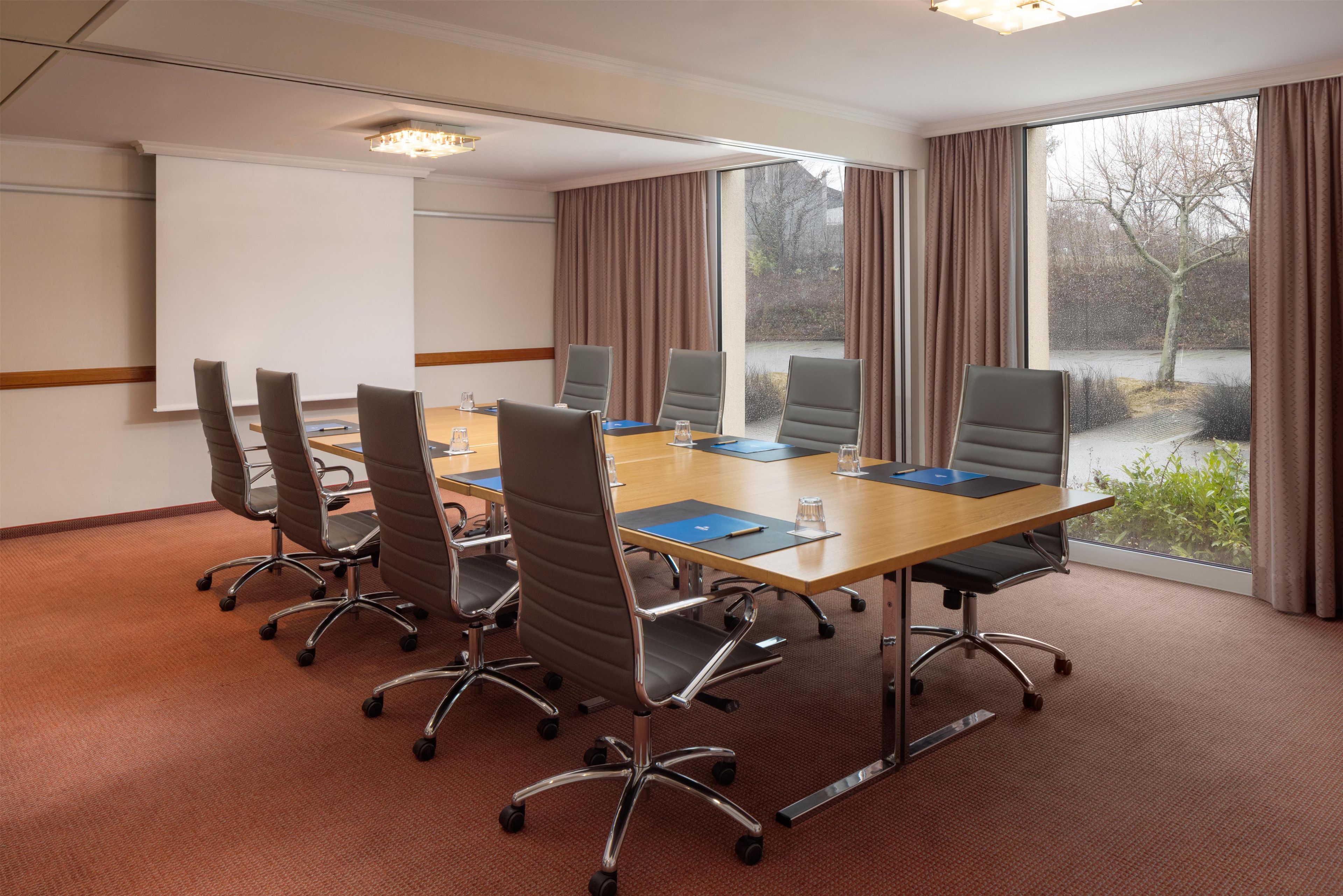 A conference room with a long table, six chairs, and a projector screen.