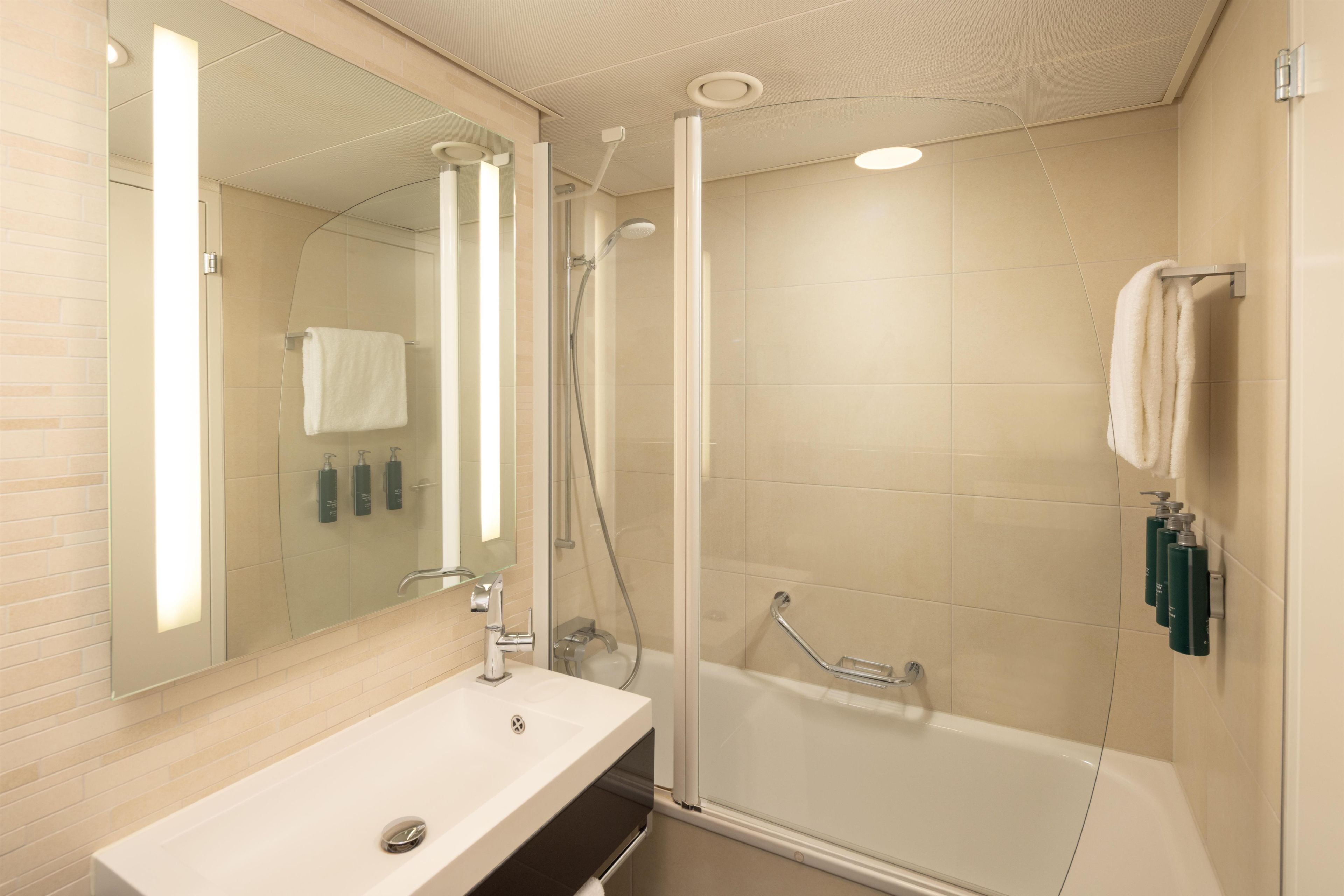 Un baño moderno con ducha envuelta en vidrio, un lavabo blanco y un espejo grande.