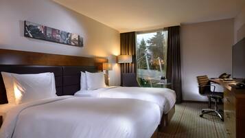 A hotel room with two beds, a desk, a chair, a lamp, and a painting on the wall.