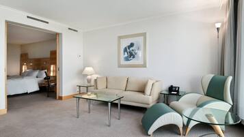 Une chambre d’hôtel avec un canapé, une table basse en verre, une lampe, une œuvre d’art encadrée au mur et un lit à l’arrière-plan.