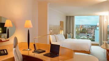 Une chambre d’hôtel avec un lit, un bureau, un ordinateur portable, une lampe et une vue sur la ville.