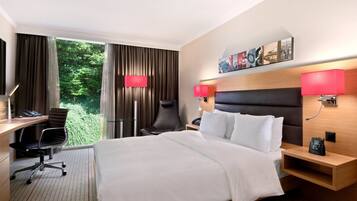 A hotel room with a large bed, a desk with a chair, a nightstand, and a wall-mounted TV.