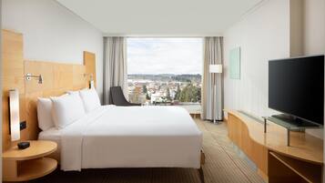 A hotel room with a large bed, a TV, a desk, and a view of a cityscape.