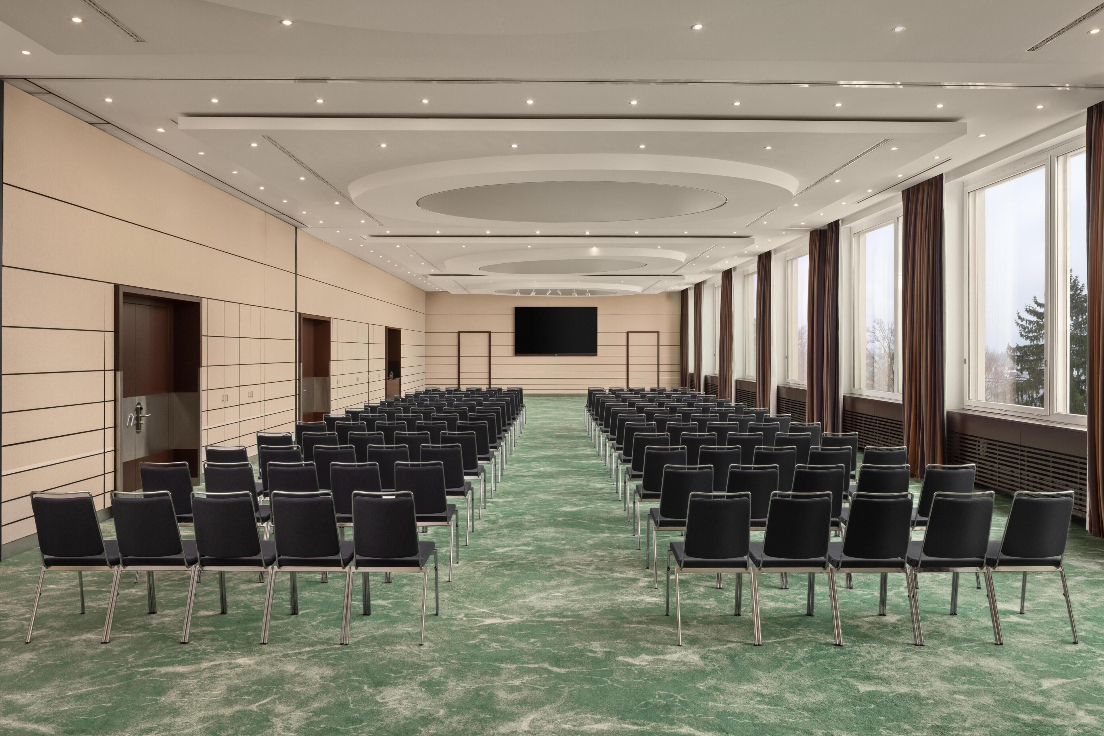 A conference room with rows of chairs, a large screen, and a view of the outdoors.