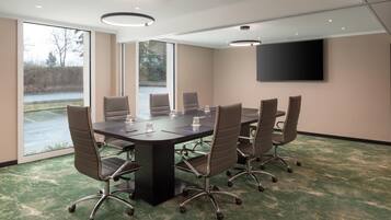 A conference room with a large table, six chairs, a flat-screen TV, and large windows.