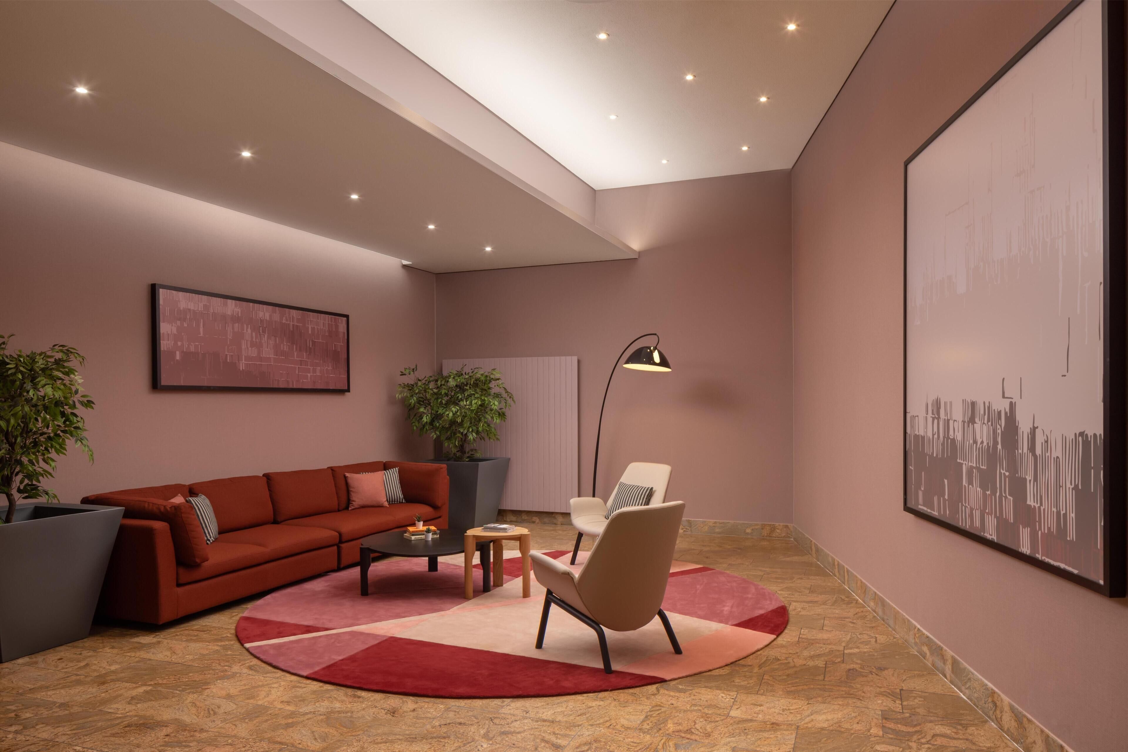 Una sala moderna con un sofá rojo, un sillón color beige, una mesita de centro y una lámpara de pie. Hay dos plantas en macetas y un cuadro abstracto grande en la pared.