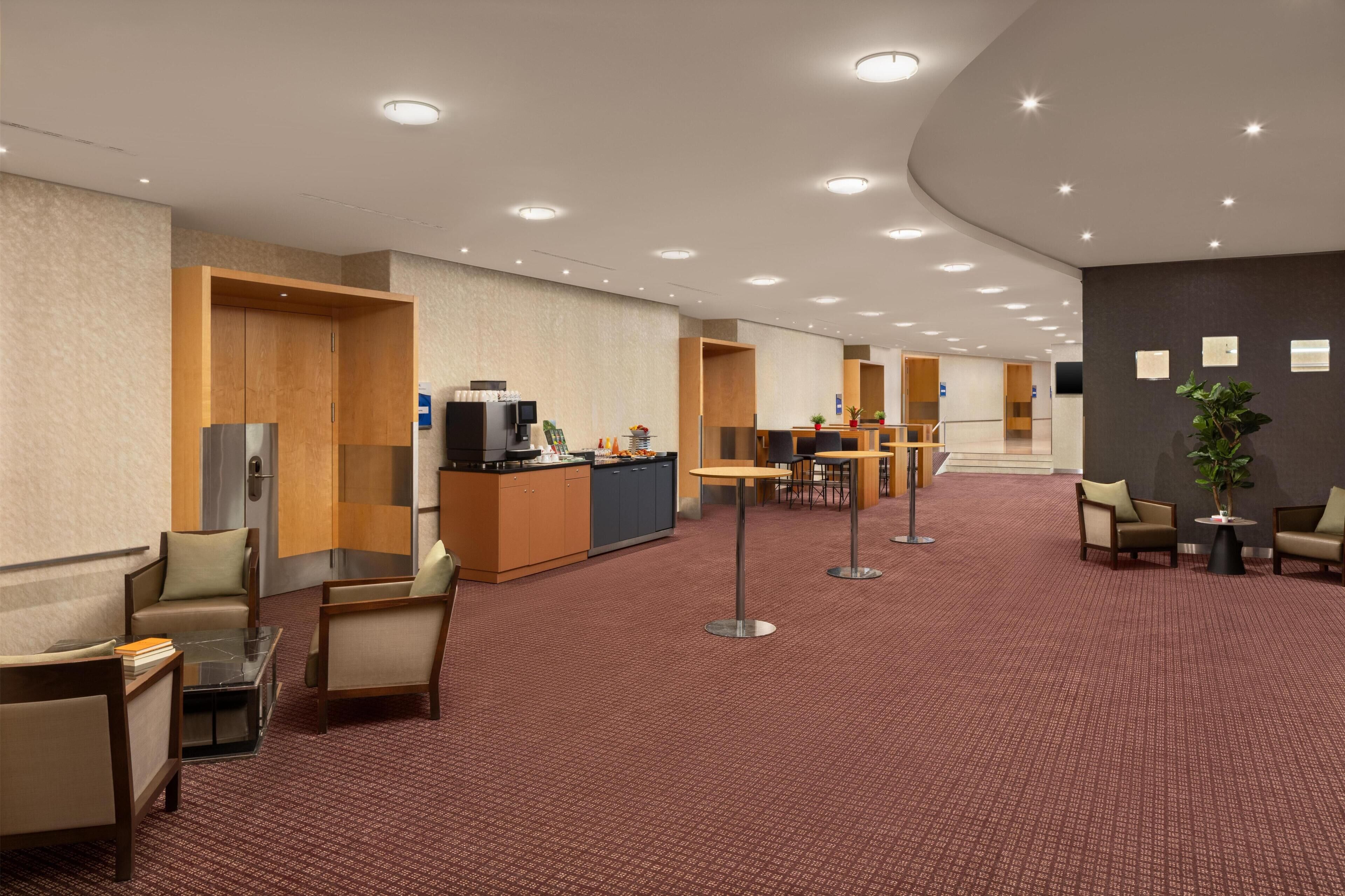 A spacious hotel lobby with a central reception desk, seating areas, and a carpeted floor.