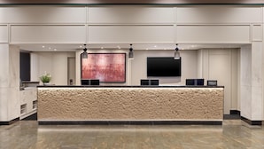 A hotel reception area with a textured counter, a large abstract painting, and a flat-screen TV. - Hilton Zurich Airport (Opfikon)