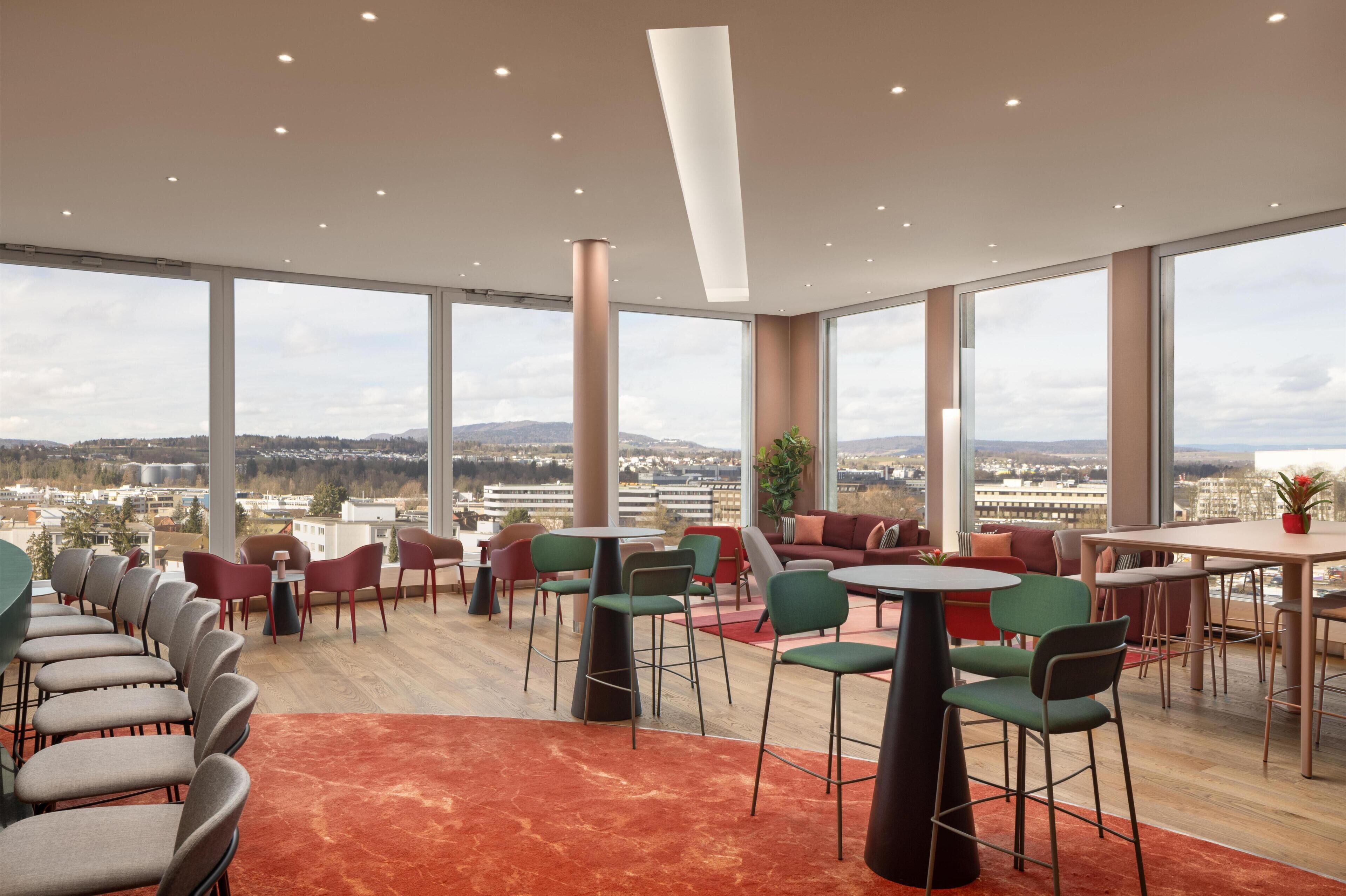 A modern lounge area with high ceilings, large windows, and a view of the cityscape.