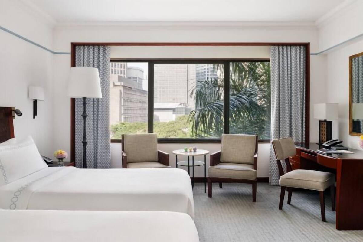 A hotel room with two beds, a desk, two chairs, a small table, and a large window with curtains.