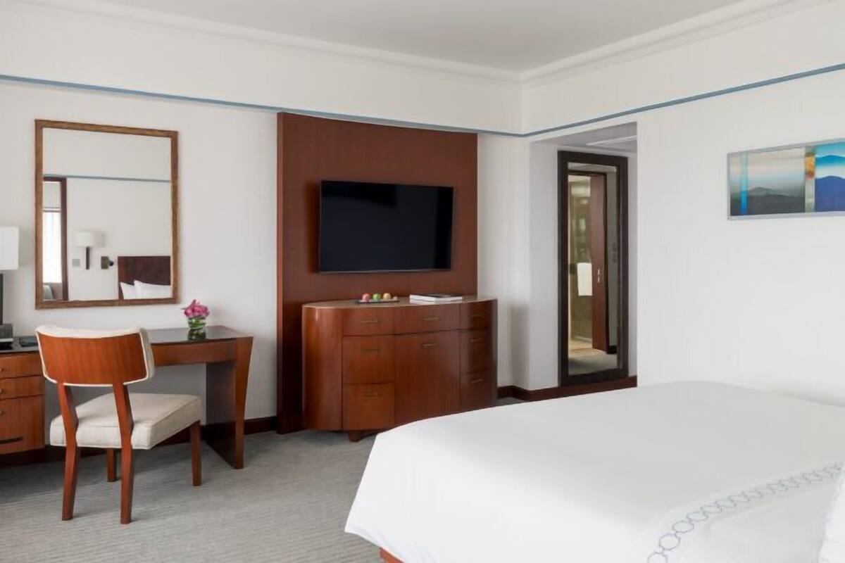 A hotel room with a bed, a desk, a chair, a television, and a door.