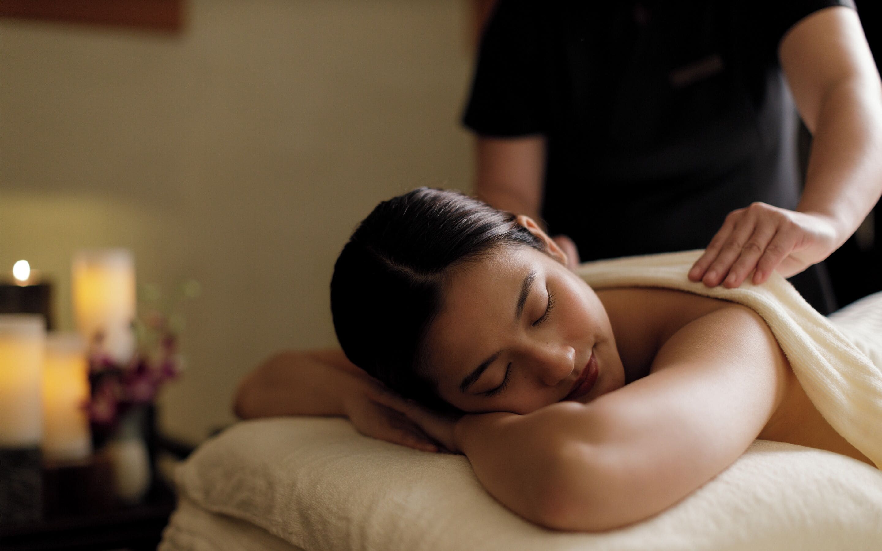 A person receiving a massage in a room with a bed, pillows, and a small table with candles.