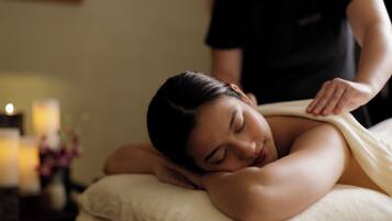 A person receiving a massage in a room with a bed, pillows, and a small table with candles.