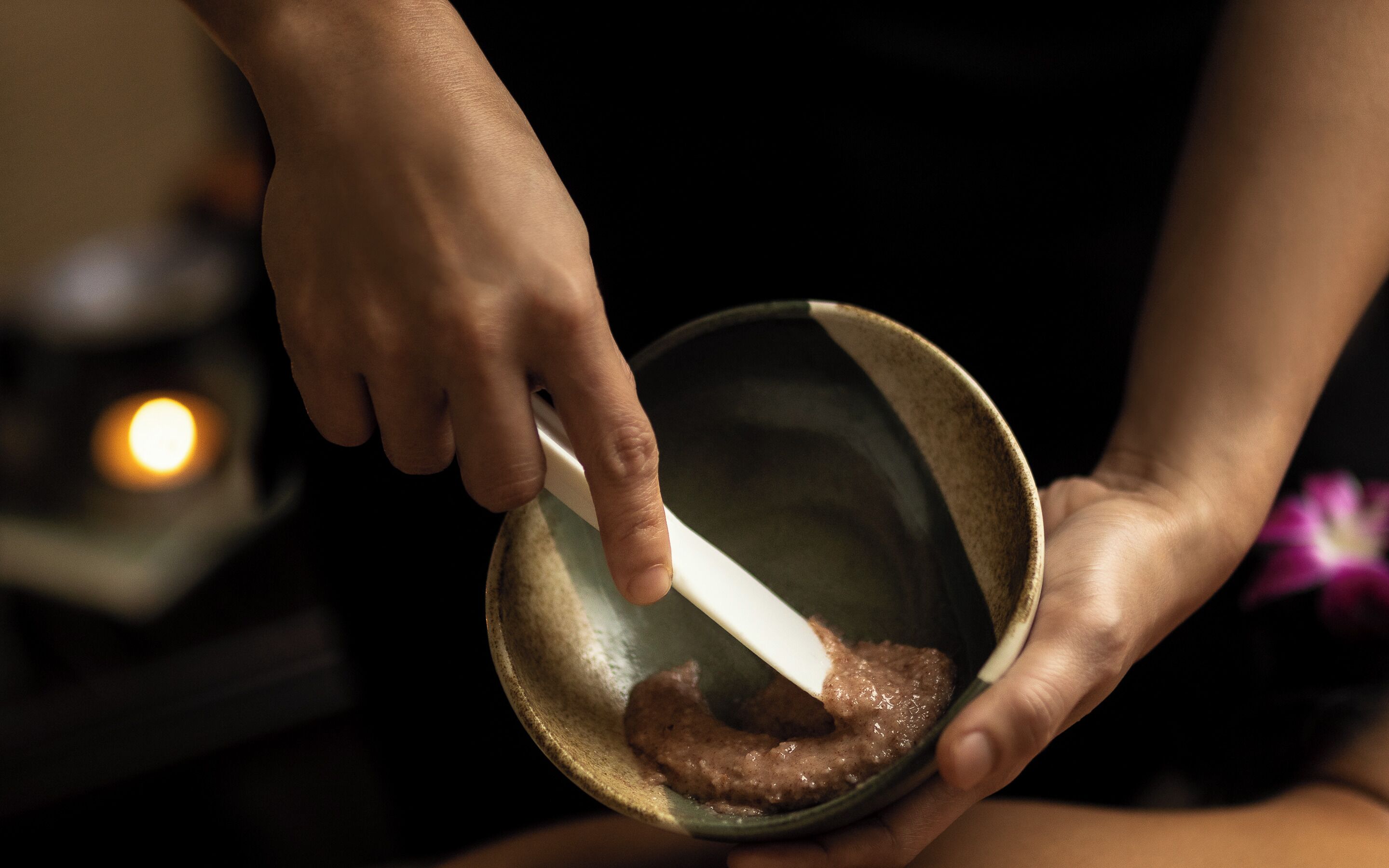 A person holding a bowl with a spoon, containing a brown mixture.