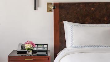 A hotel room with a bed, a nightstand with a telephone and a vase of flowers, and a wall-mounted security camera.