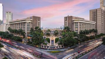 A multi-story hotel with a central courtyard, surrounded by palm trees and modern buildings.