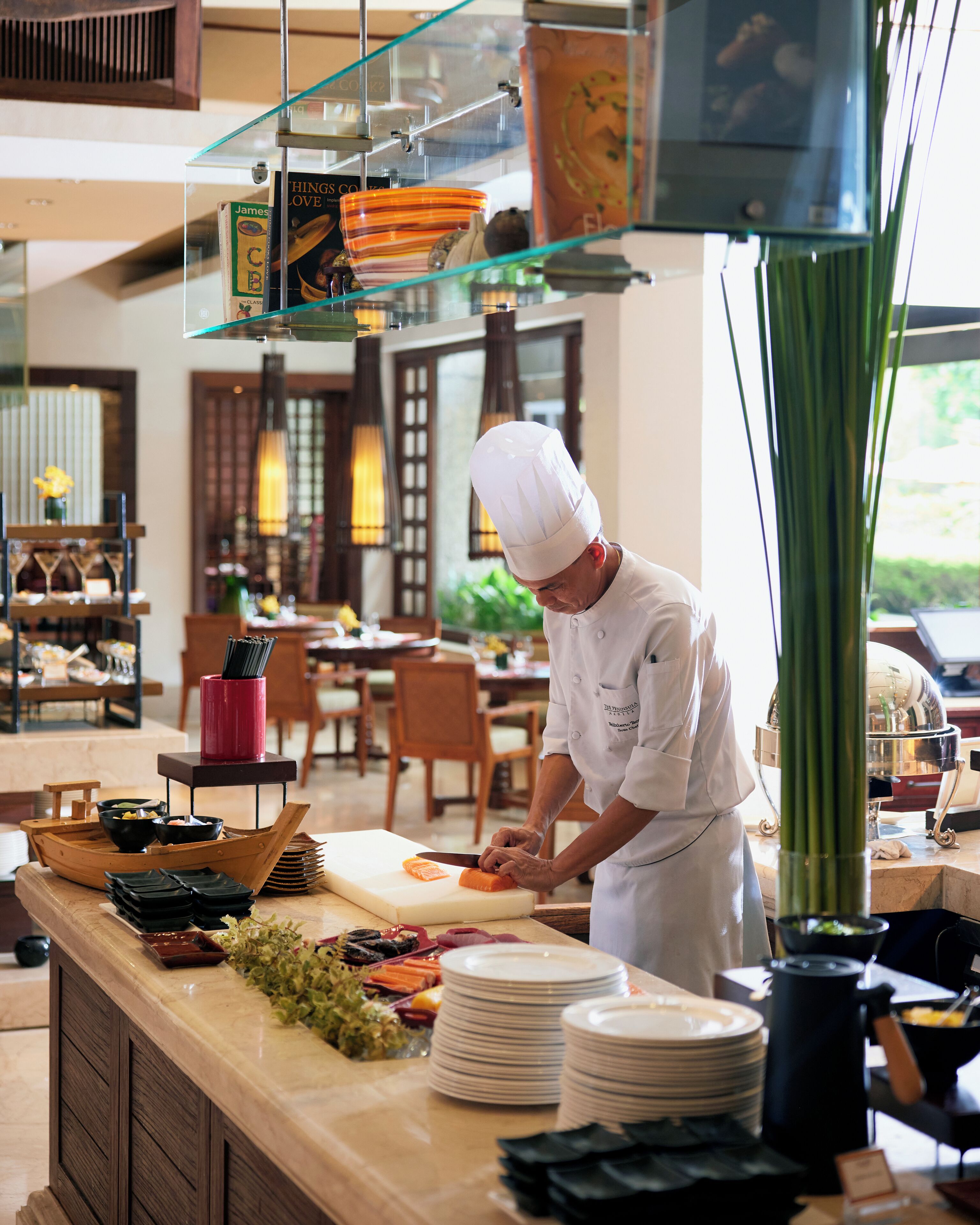 A chef preparing food in a well-lit kitchen with a modern design, featuring wooden elements and a variety of cooking utensils and ingredients.