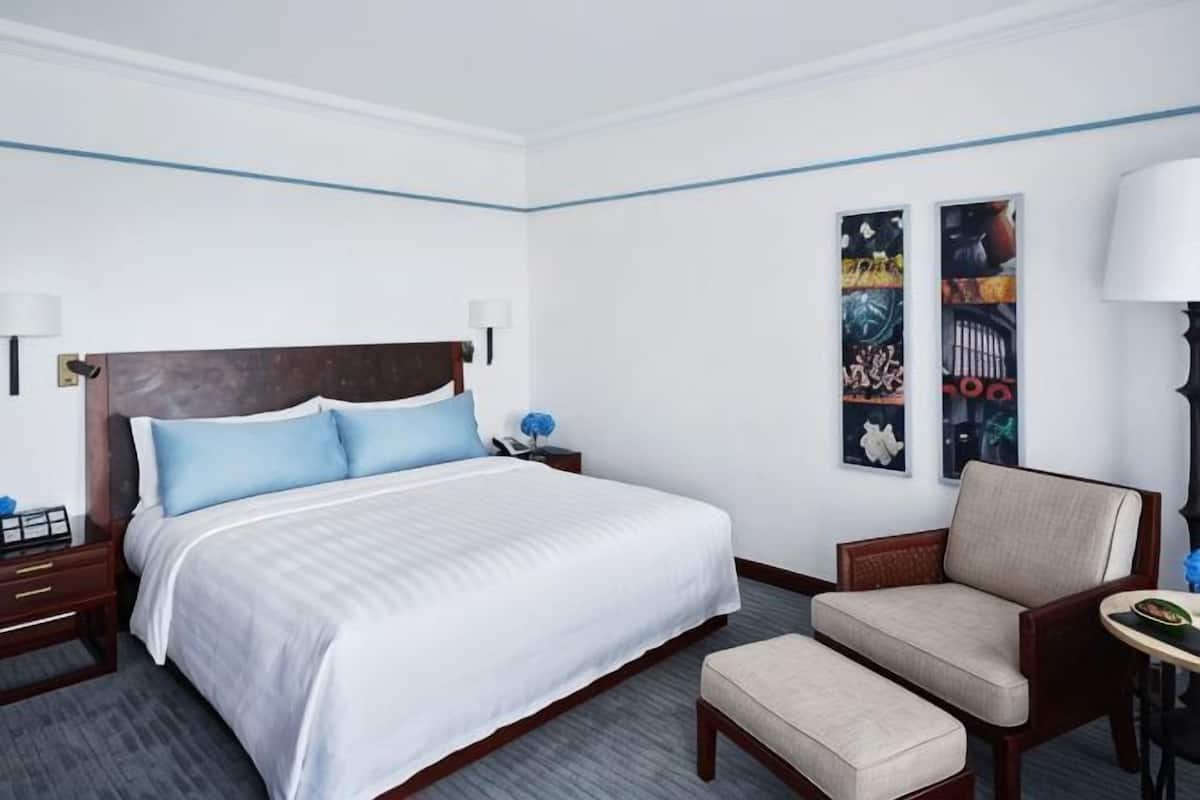 A hotel room with a large bed, a chair, a desk, and two wall-mounted lamps.
