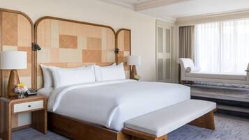 A hotel room with a large bed, two bedside tables with lamps, a bench, a chair, and a window with curtains.