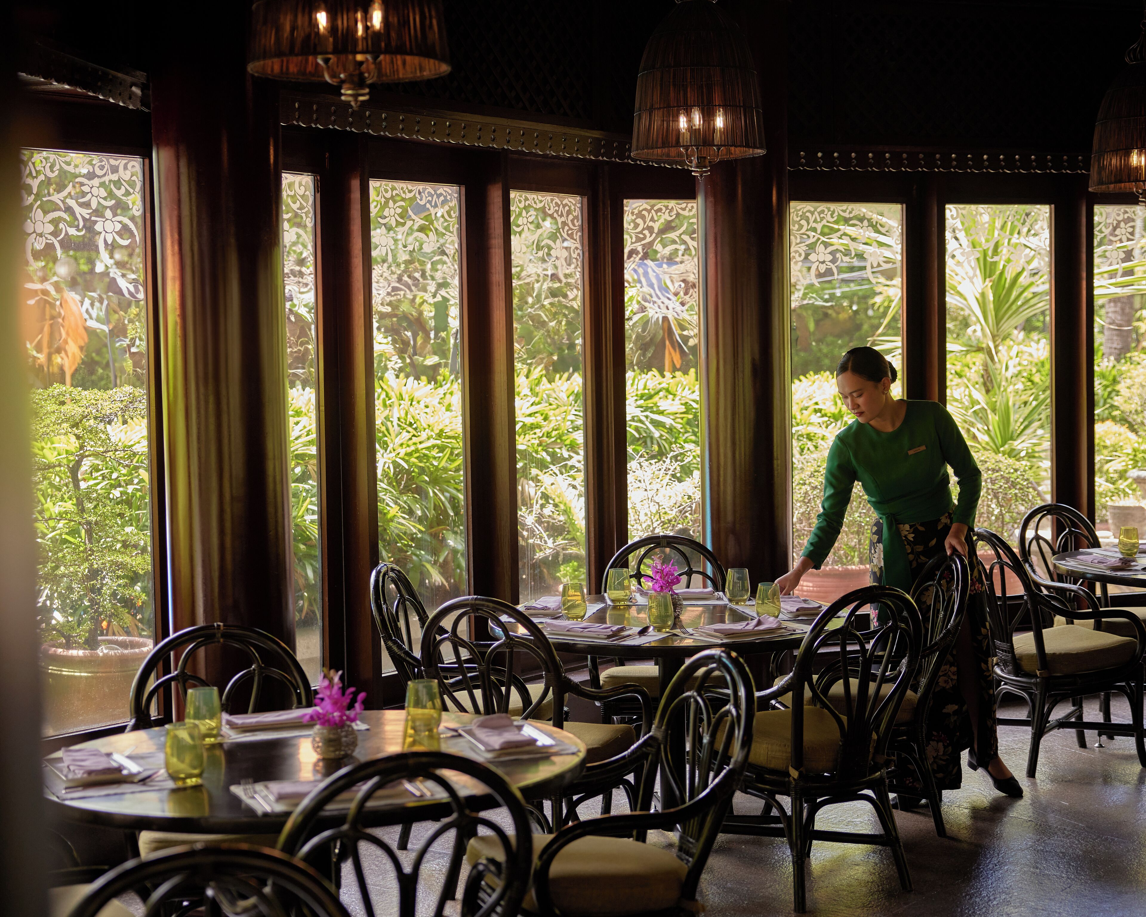 A restaurant with large windows, tables set with chairs, and a person attending to the tables.