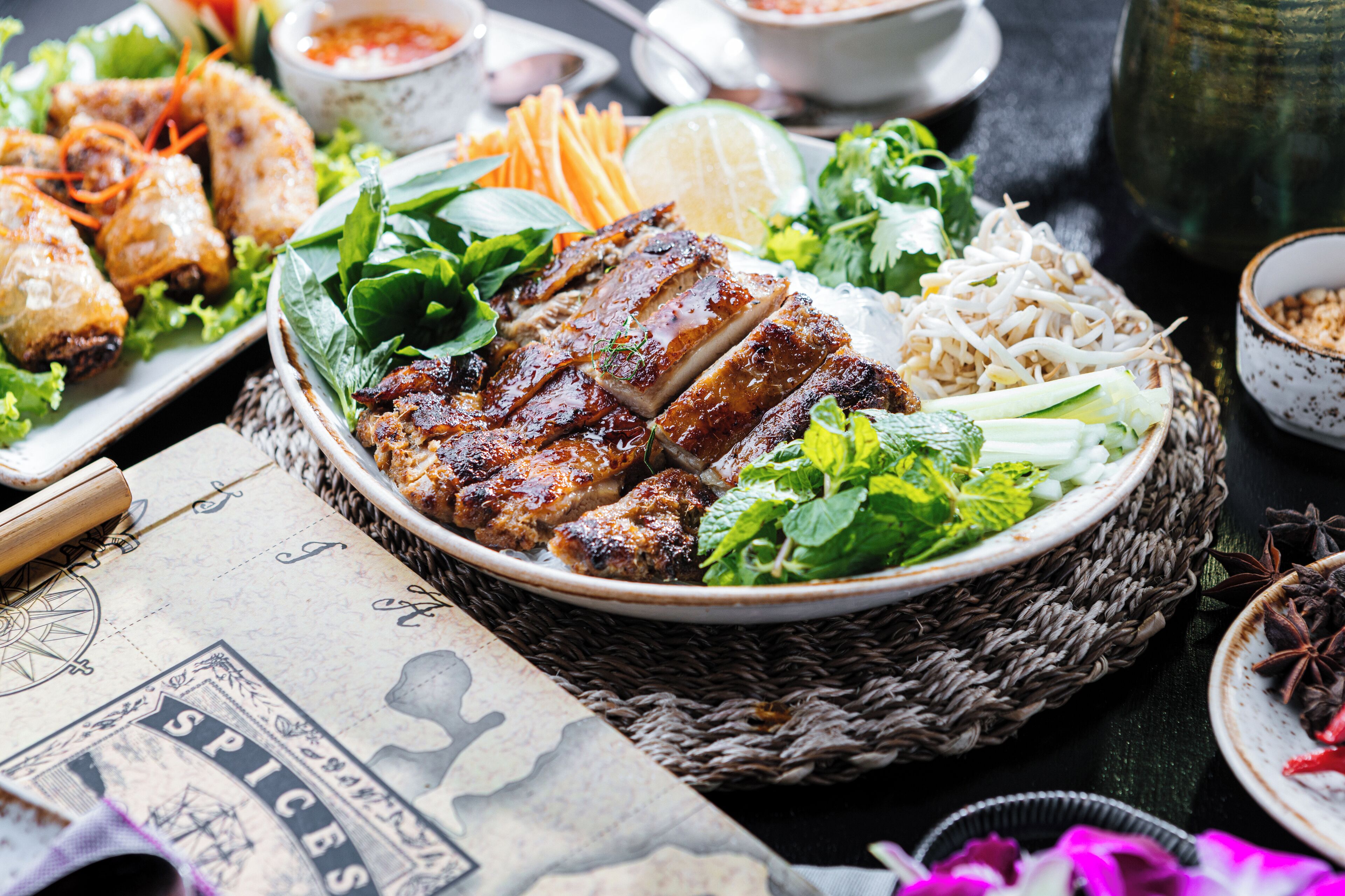 A table with various dishes including grilled meats, vegetables, and noodles, suggesting a meal setting.