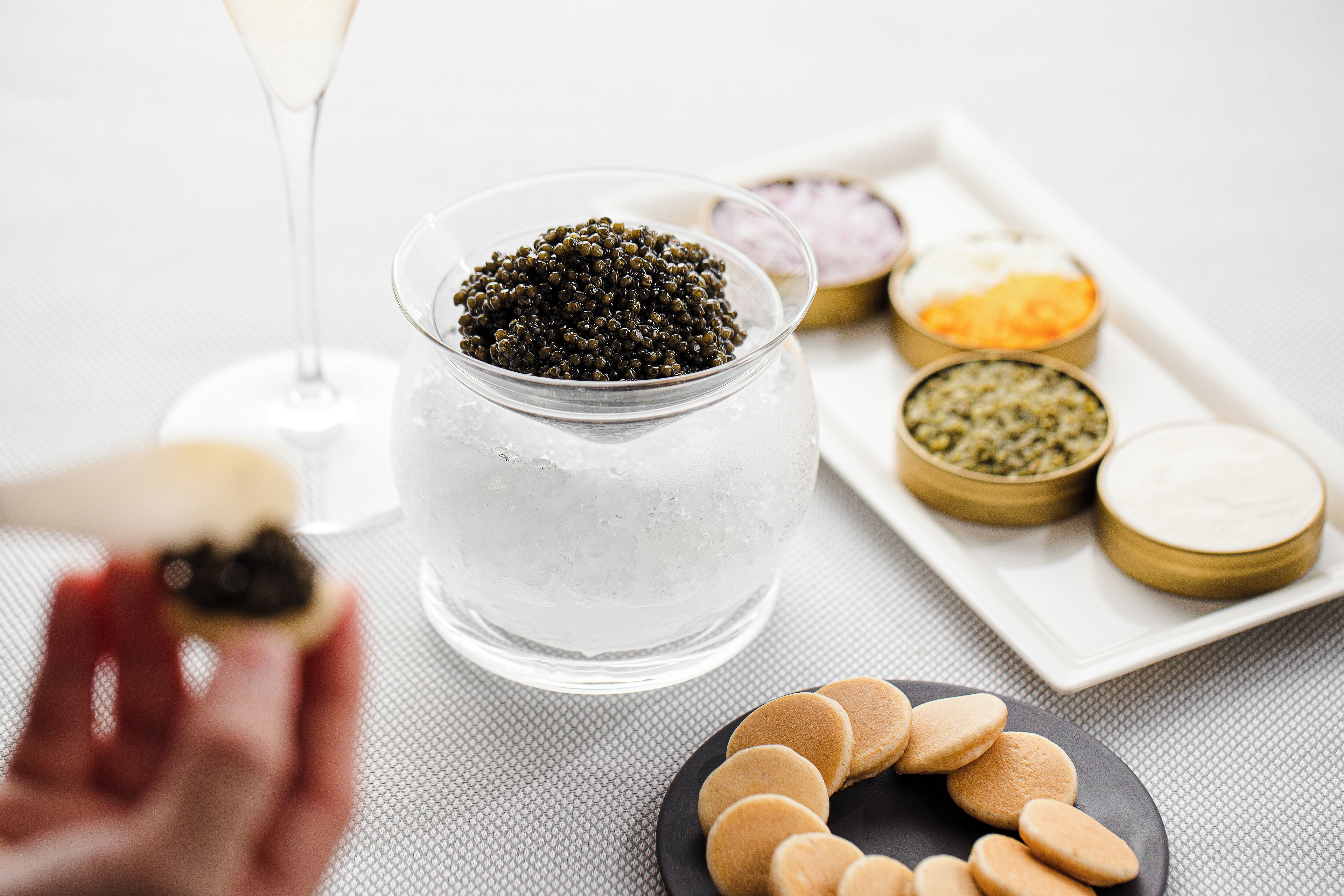 A glass of water with ice, a jar of black caviar, and a plate of cookies on a table.