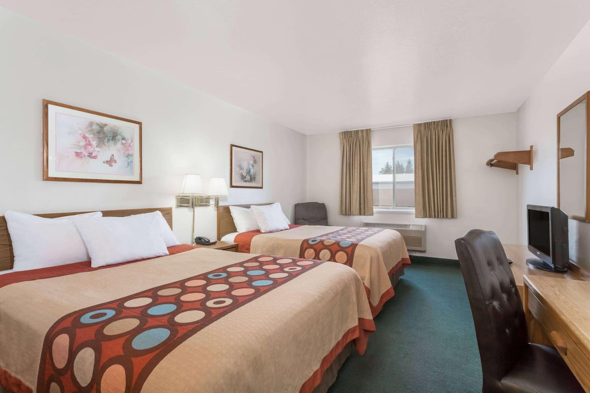 Une chambre d’hôtel avec deux lits, un bureau avec une télévision, une chaise et une fenêtre avec des rideaux.