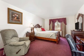 Ein Hotelzimmer mit einem Bett, einem Sessel, einem Schreibtisch, einem Fernseher und einem gerahmten Bild an der Wand.