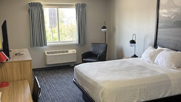 Une chambre d’hôtel avec un lit, un bureau, une chaise, une lampe et une fenêtre avec des rideaux.
