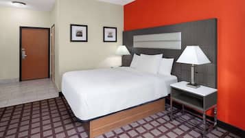 Quarto de hotel com uma cama, duas luminárias, uma mesa de cabeceira e uma porta.