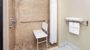 A shower area with a white chair, grab bars, a towel rack, and a showerhead.