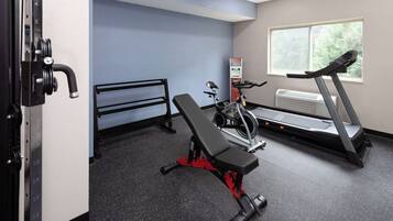 A gym with a bench press, a treadmill, and a wall-mounted weight rack.
