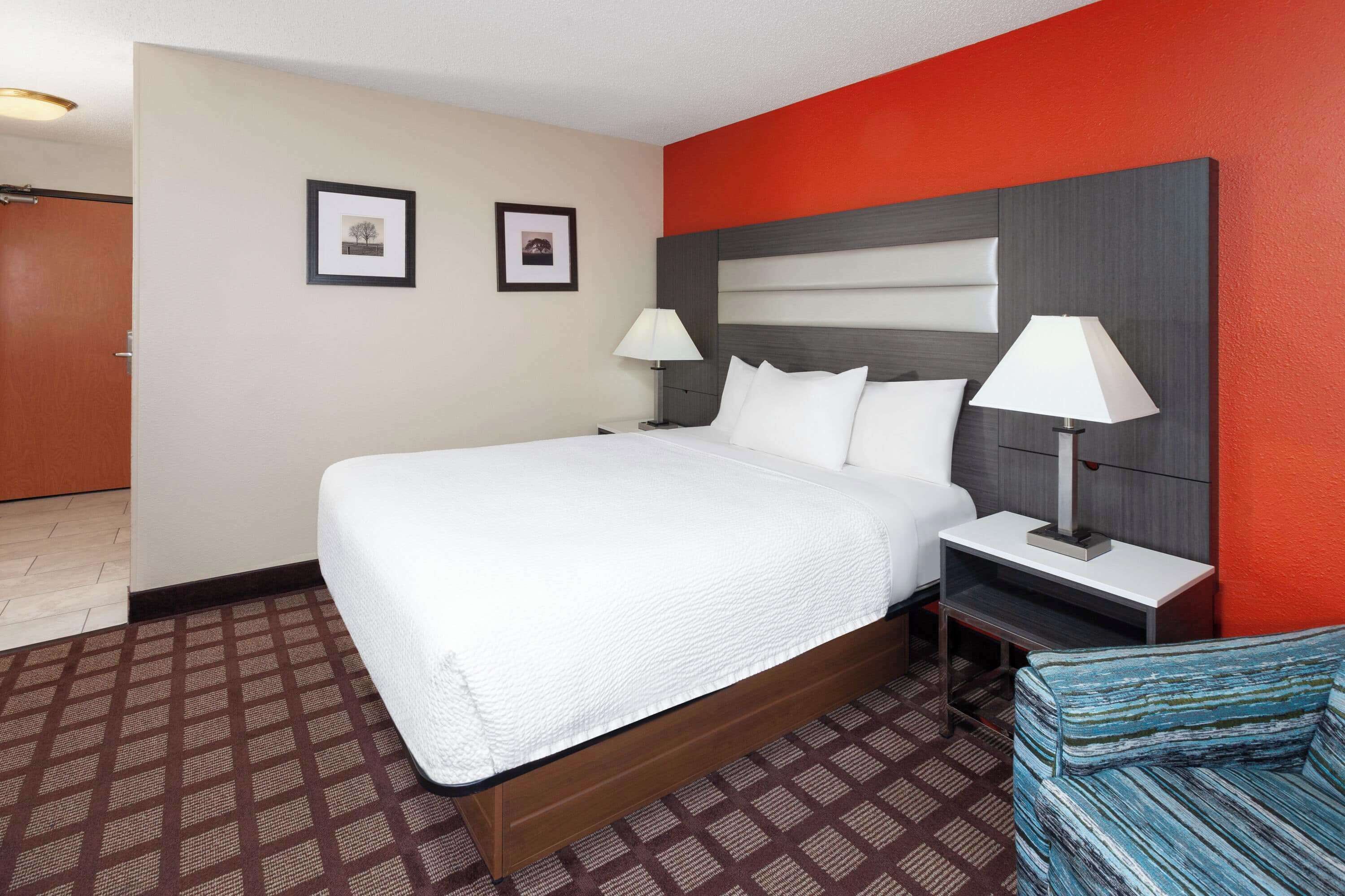 A hotel room with a large bed, two bedside tables, a nightstand, a sofa, and a red accent wall.