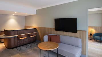 Una sala de estar moderna con un sofá, una mesa redonda de centro, un televisor montado en la pared y una zona de bar con taburetes.