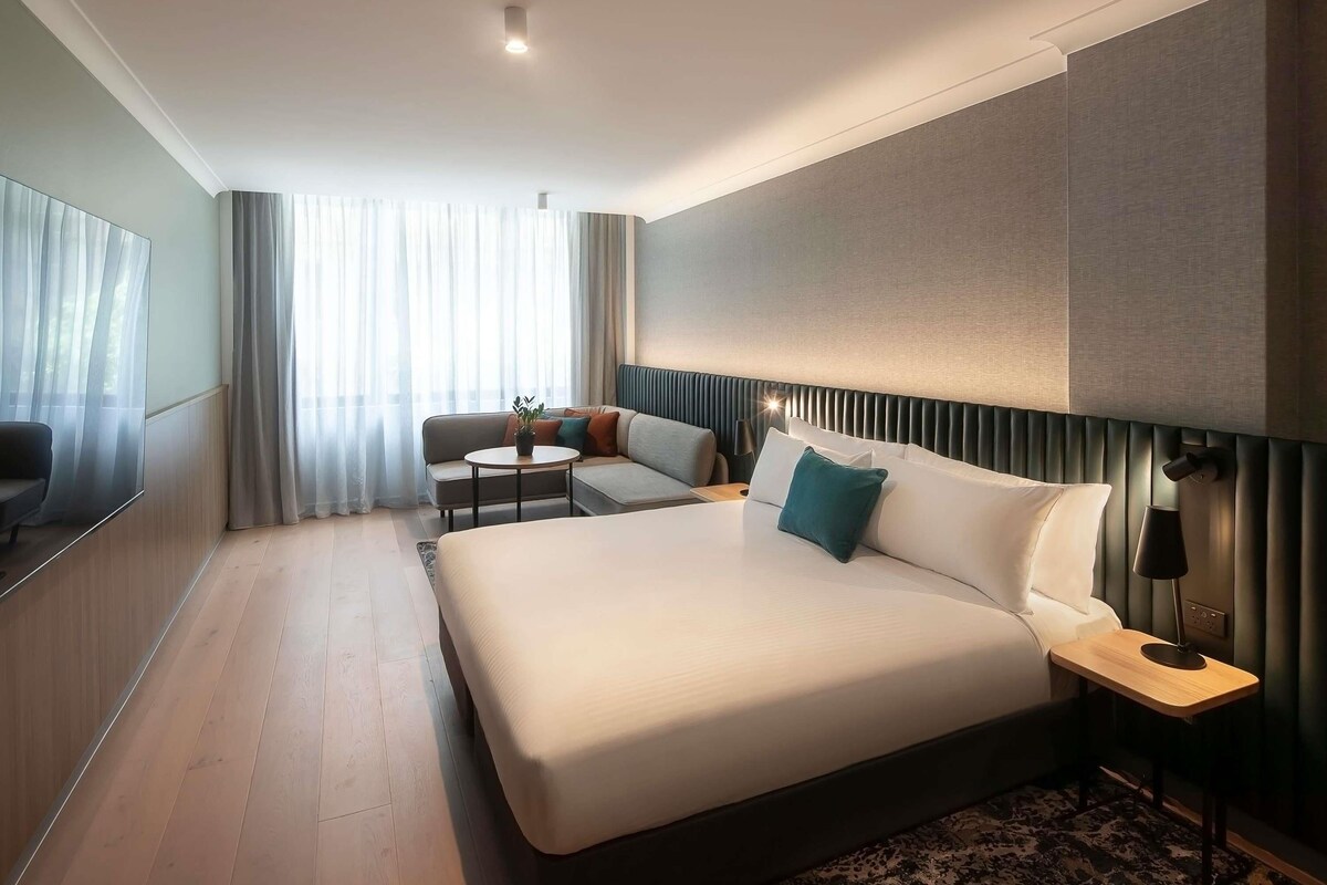 A modern hotel room with a large bed, a sofa, a small table, and a TV.