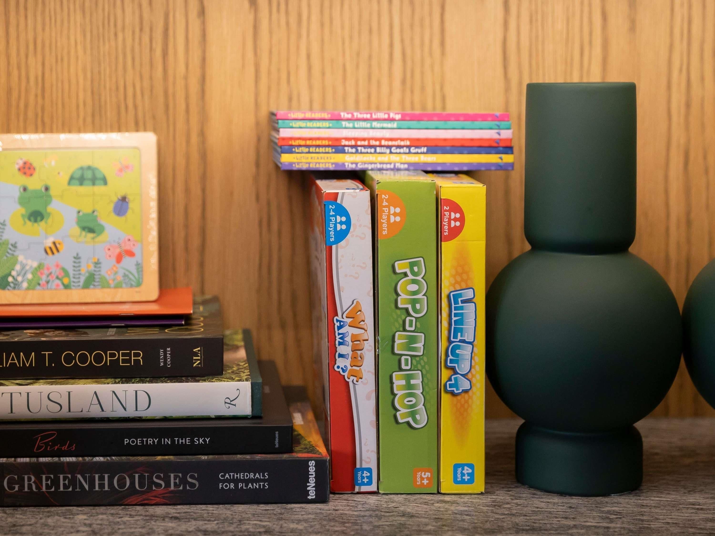 Una pila de libros, un rompecabezas y dos cajas de juegos sobre una estantería.
