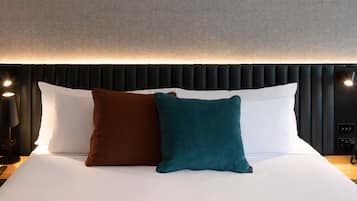 A neatly made bed with white sheets, two pillows (one brown and one teal), and a black headboard with a textured design.